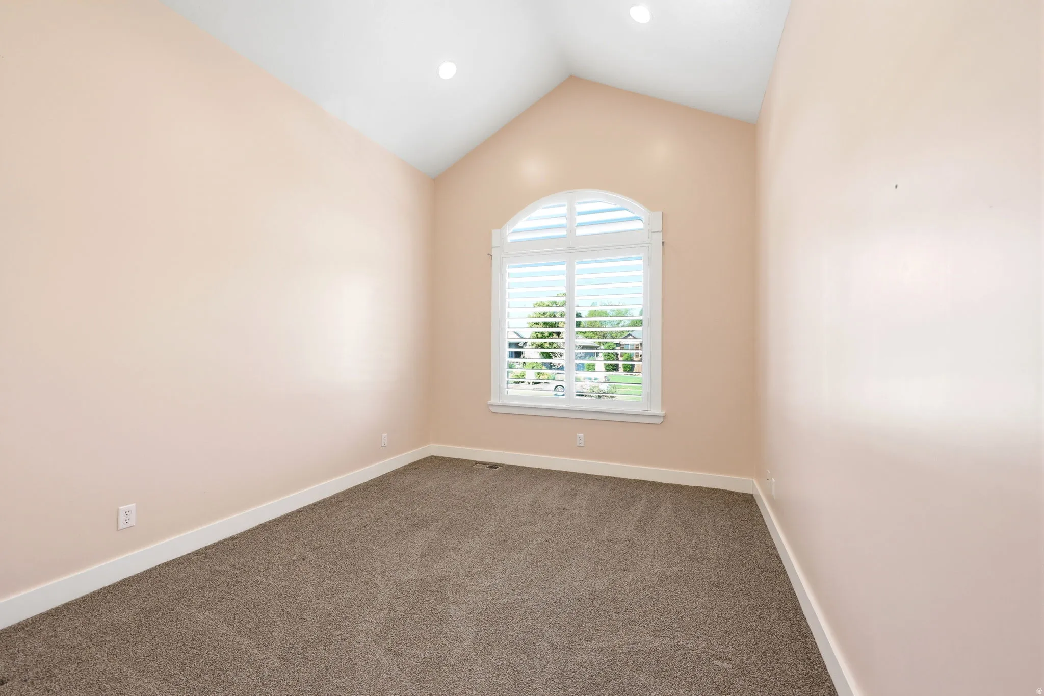 Room featuring an arched window with plantation shutters, vaulted ceiling, recessed lighting, and neutral carpeting
