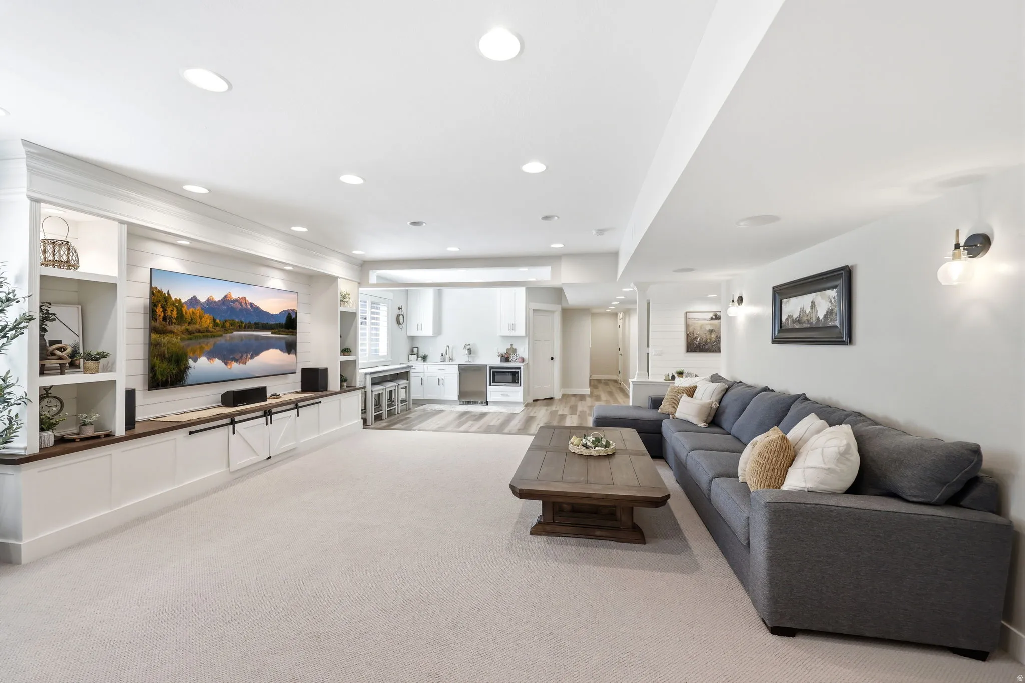 Spacious entertainment area featuring recessed lighting, a built-in media console with barn door accents, and shelving