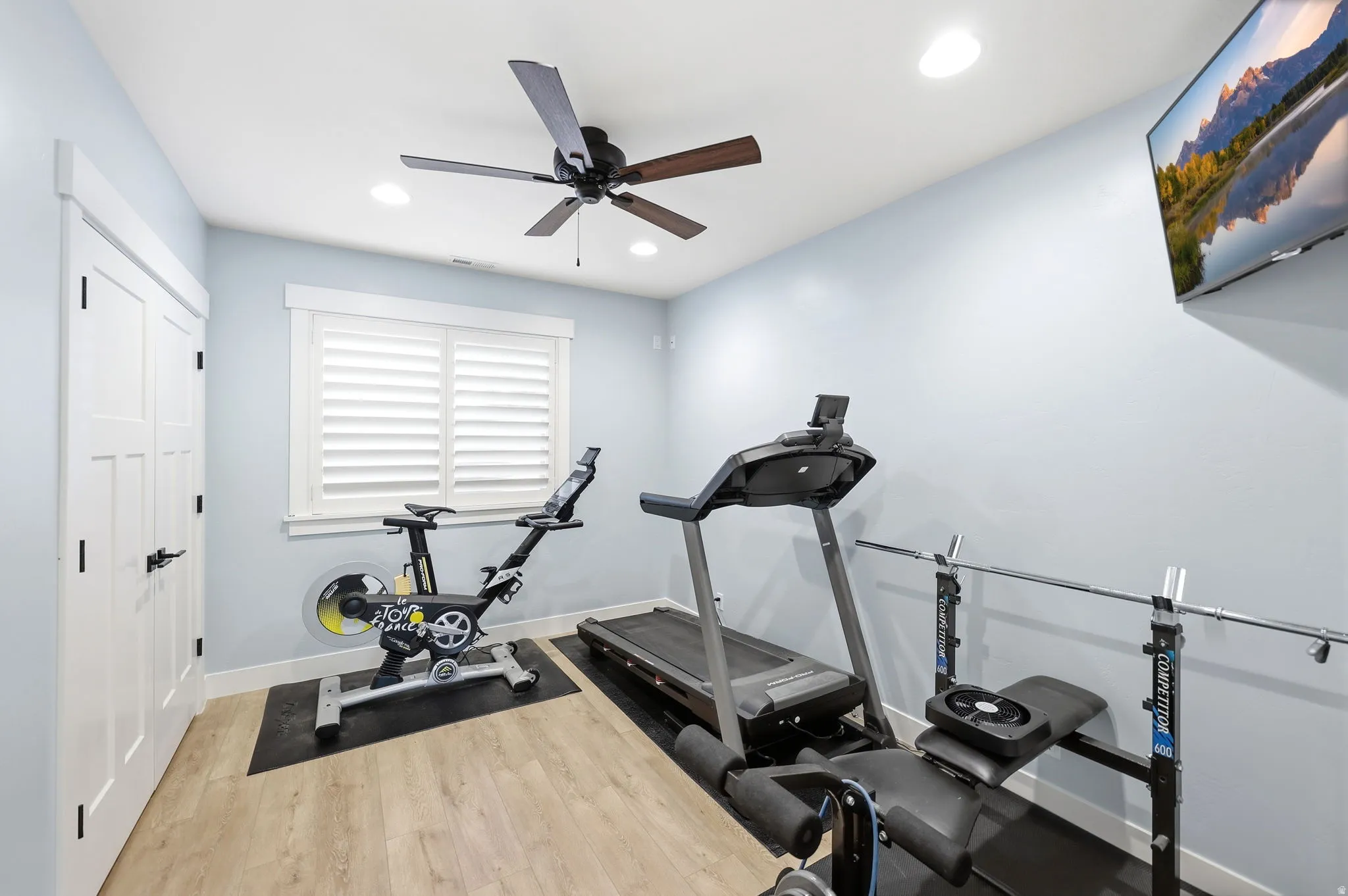 Recessed lighting illuminates this versatile room, featuring a ceiling fan, light wood-finish flooring, and a window with plantation shutters