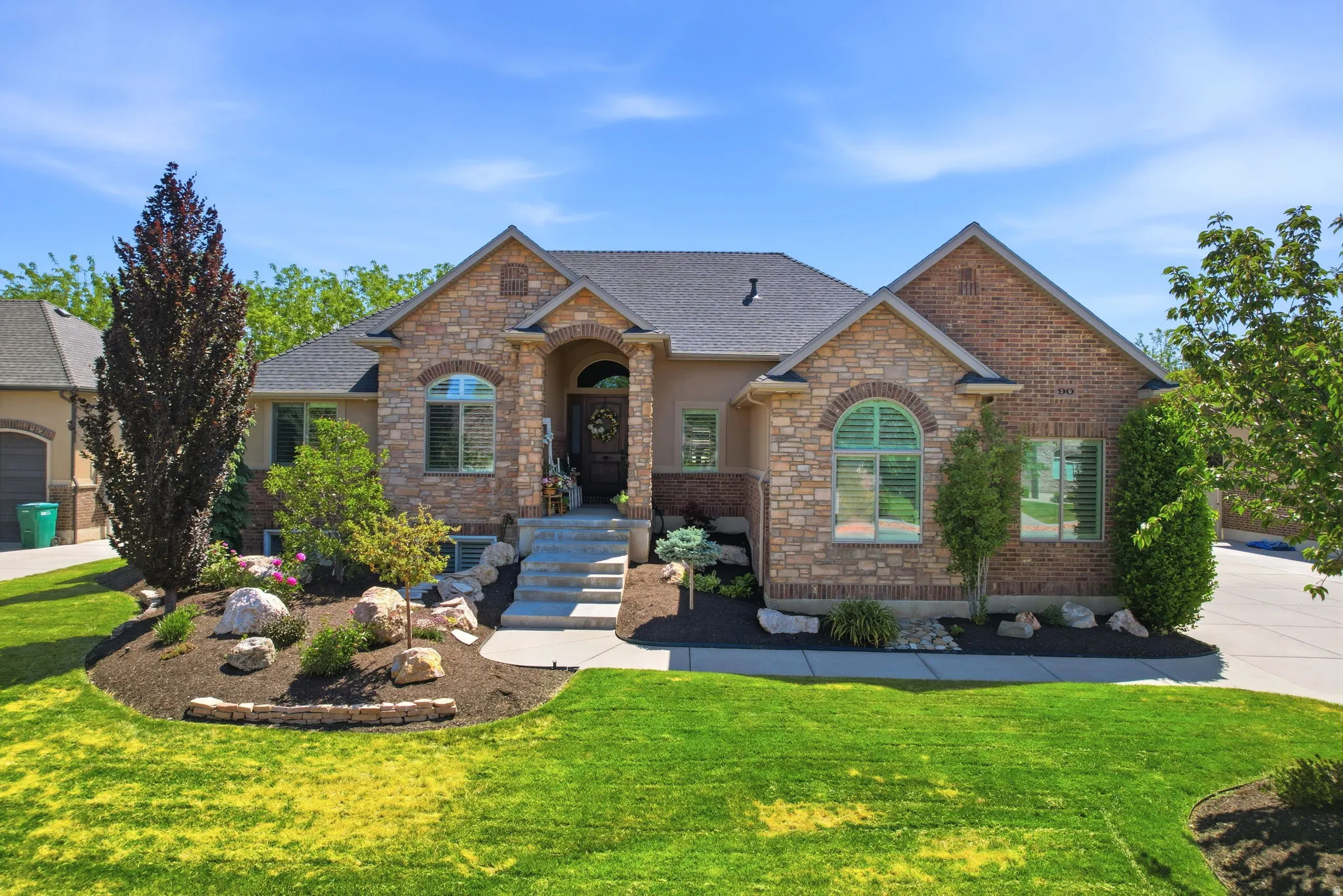 Stone and brick facade with arched entryway, complemented by a gabled roofline and landscaped front yard