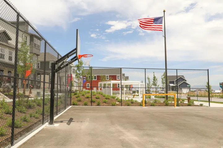 Outdoor sport court featuring an asphalt surface, chain-link fencing, a basketball hoop, and a small yellow goal