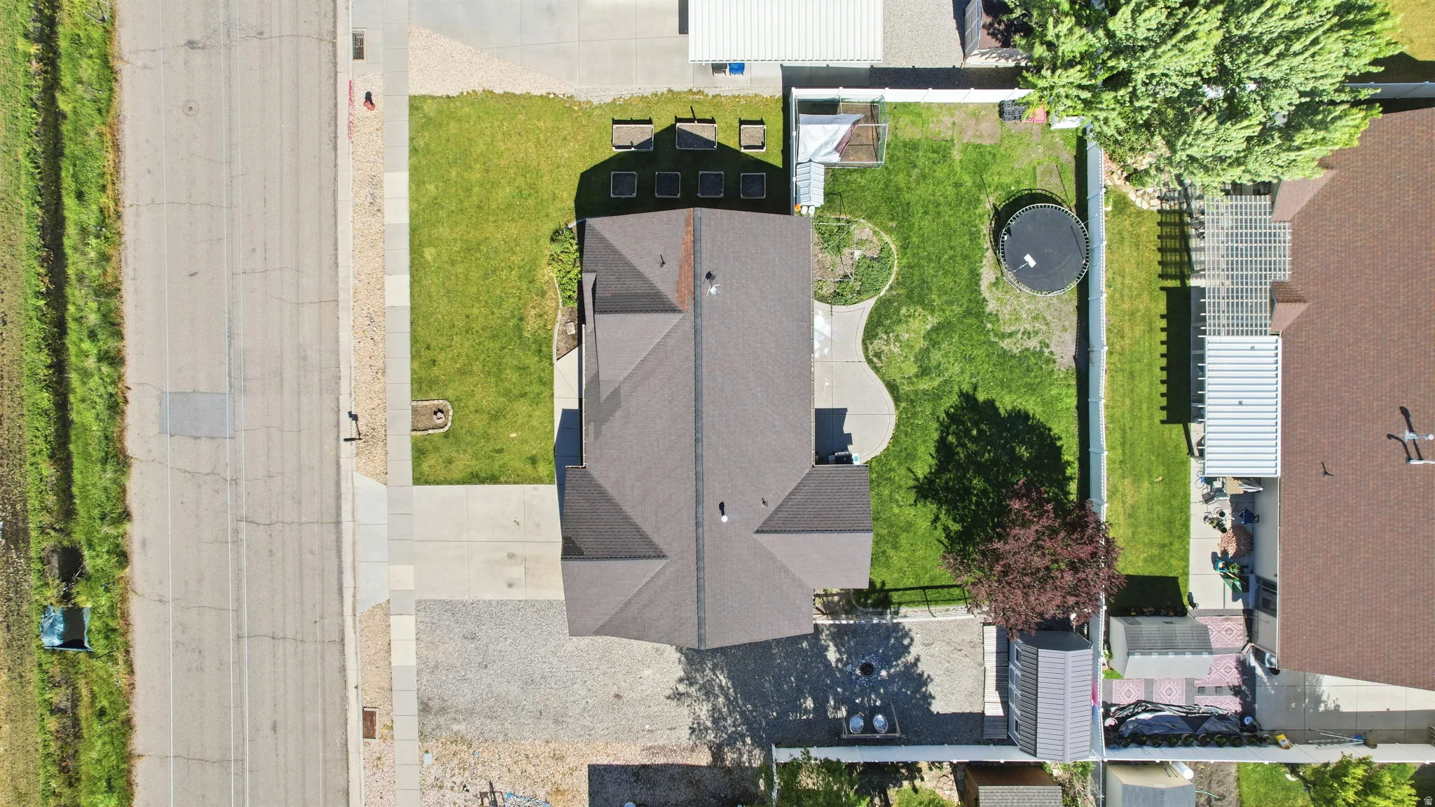 Aerial view of the property featuring a dark-toned shingle roof, a large grassy backyard with concrete pathways, and a gravel driveway