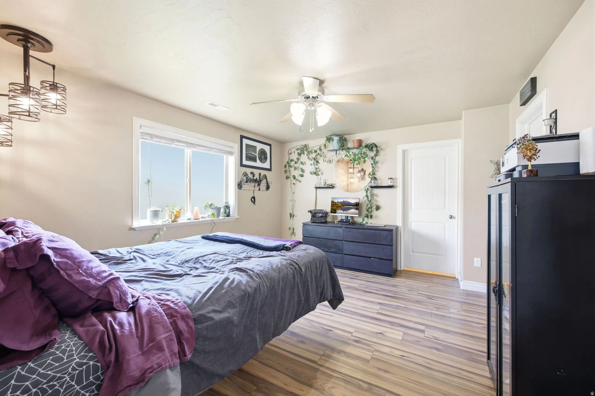 Spacious room featuring wood-finish flooring, a large window, a ceiling fan, and a light fixture with decorative metal cages
