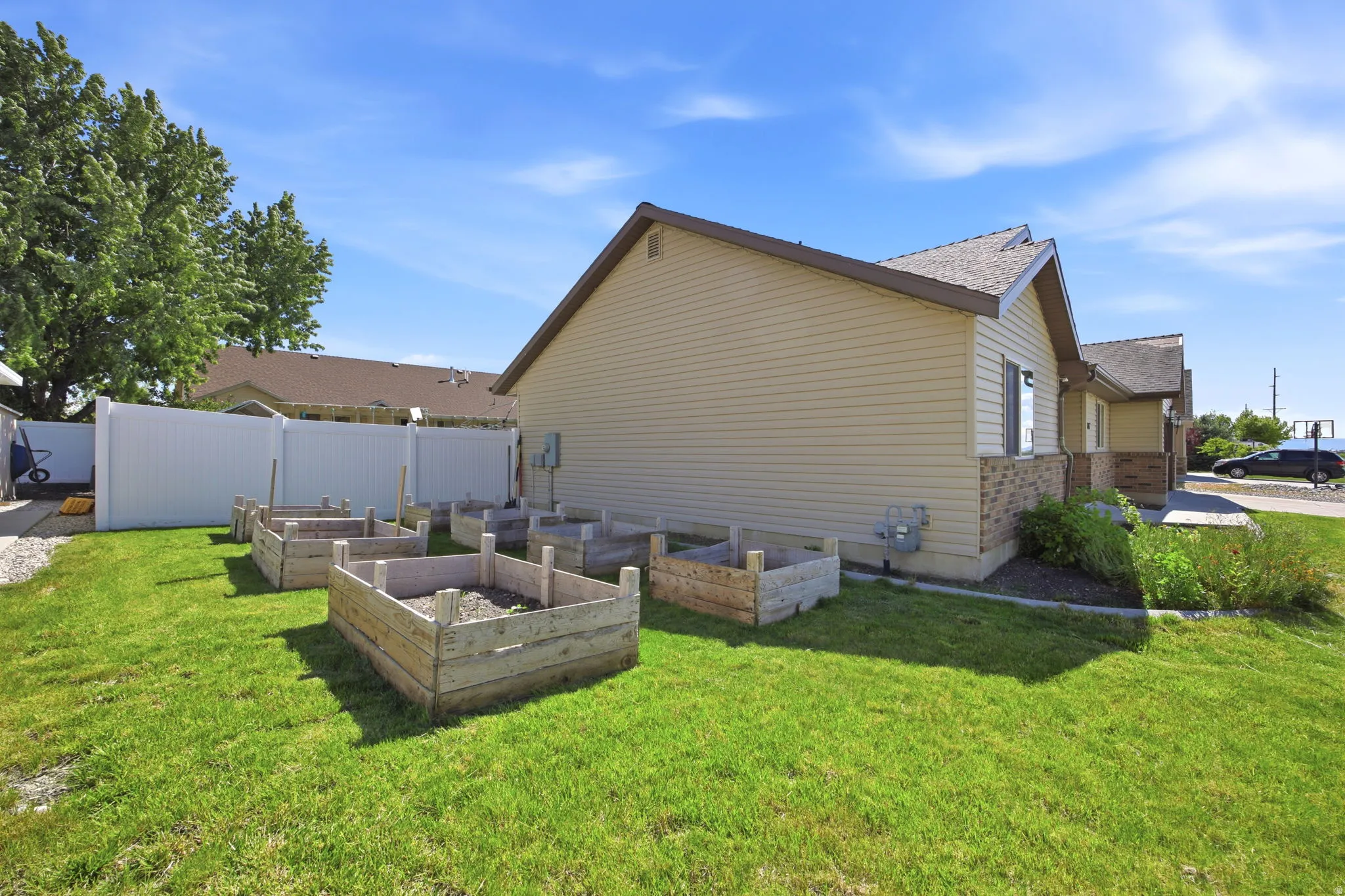 Rear yard with five raised garden beds on a manicured lawn, featuring a full privacy fence and a two-tone exterior with siding and brick accents