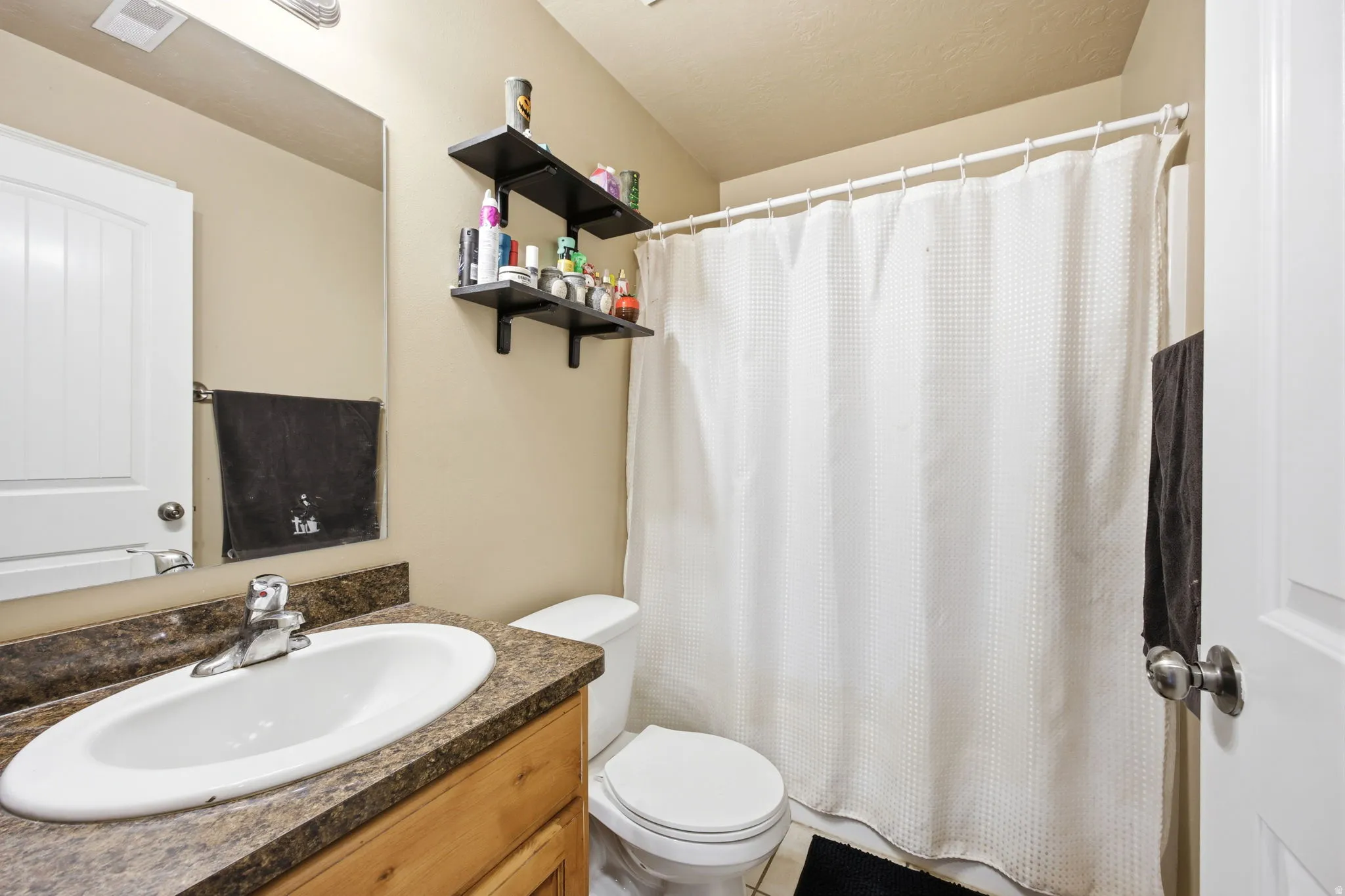 Bathroom featuring a wood-finish vanity with a built-in sink, a speckled countertop, a large wall mirror, and a white shower curtain