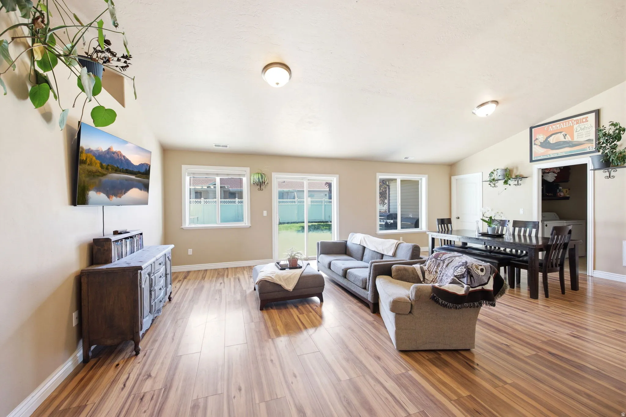 Spacious open-concept living area featuring wood-finish flooring, a vaulted ceiling, recessed lighting, and multiple windows