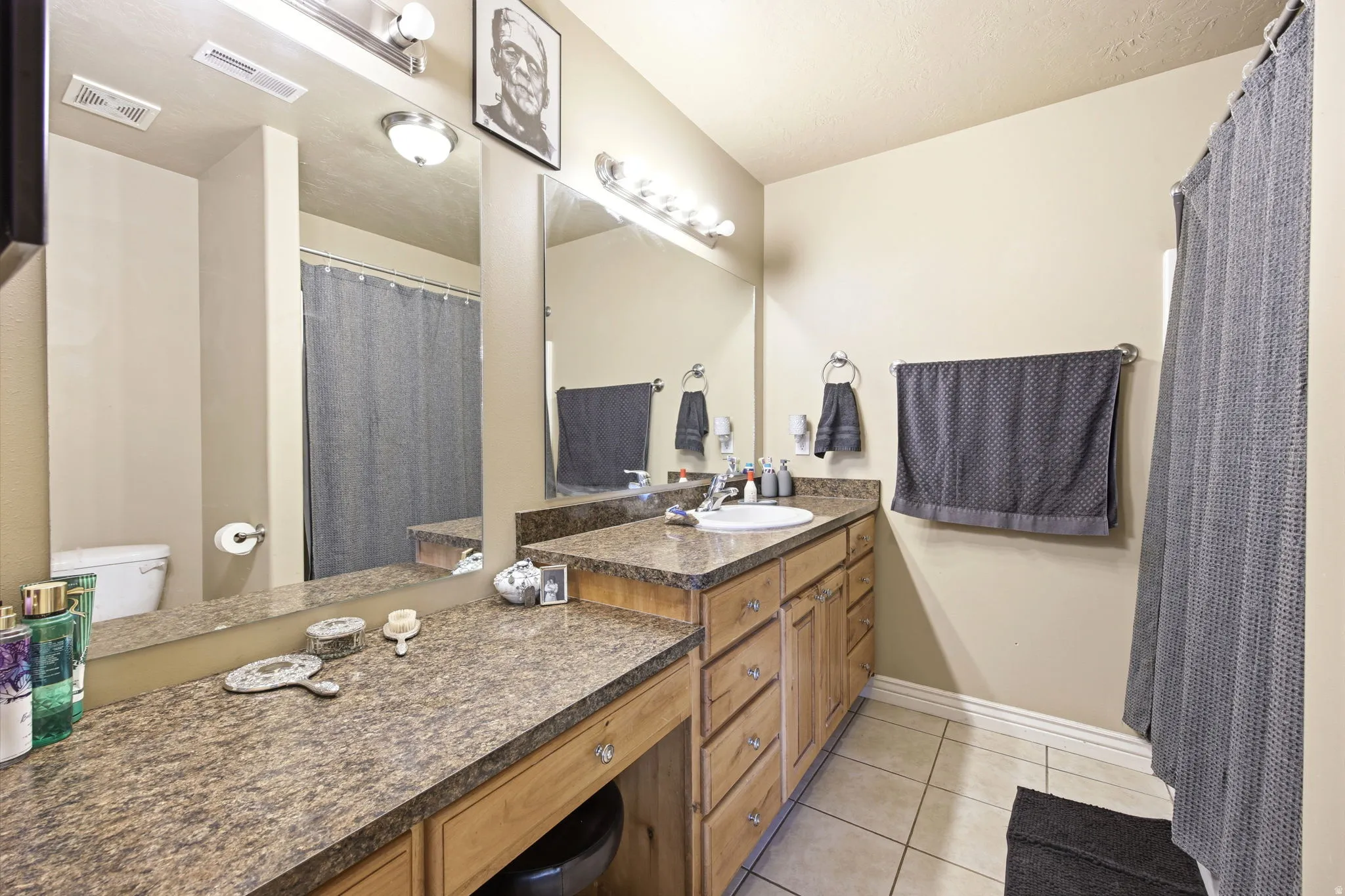 Bathroom featuring a double vanity with light wood cabinetry, a built-in makeup vanity, and a shower with a privacy curtain