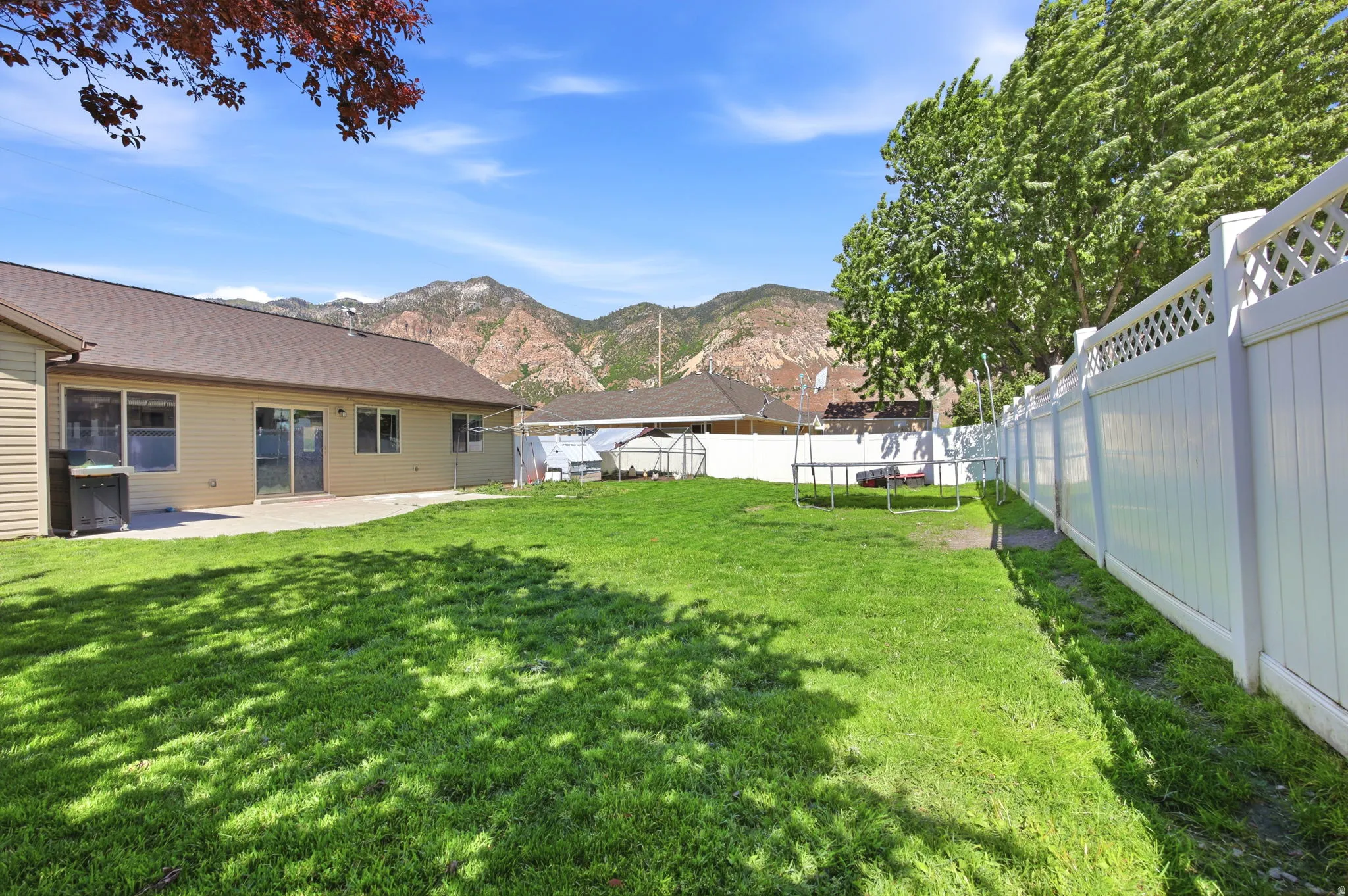Expansive rear yard featuring green lawn, a broad patio, and a white lattice-top fence