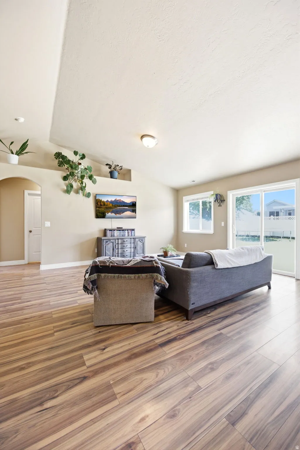 Spacious living area featuring vaulted ceilings, wood-finish flooring, and light neutral wall tones
