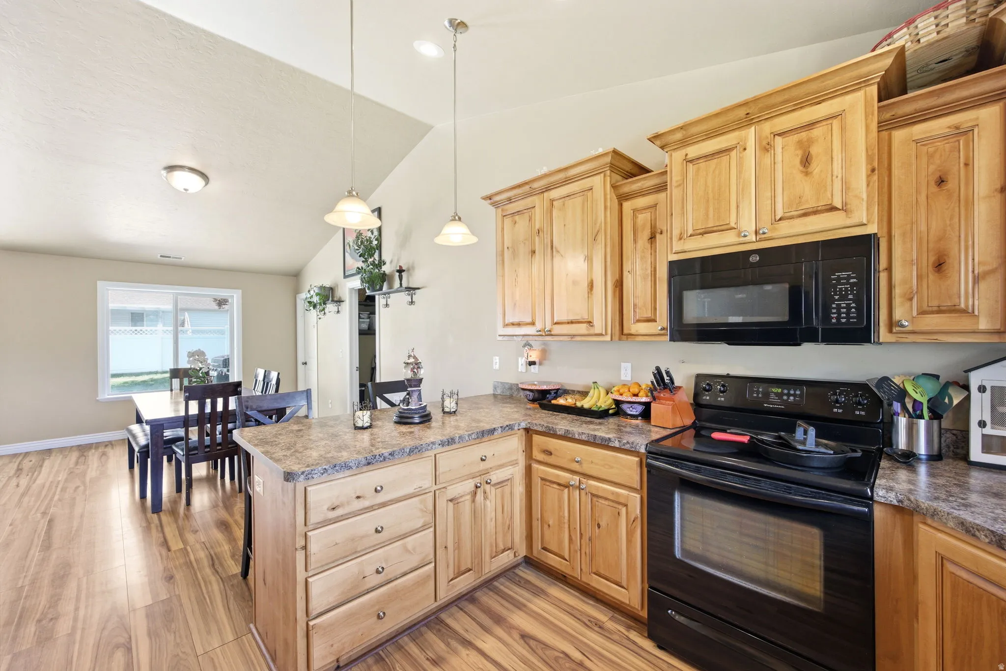 Kitchen featuring wood-finish flooring, light wood cabinetry, stone-finish countertops, black appliances, and a vaulted ceiling