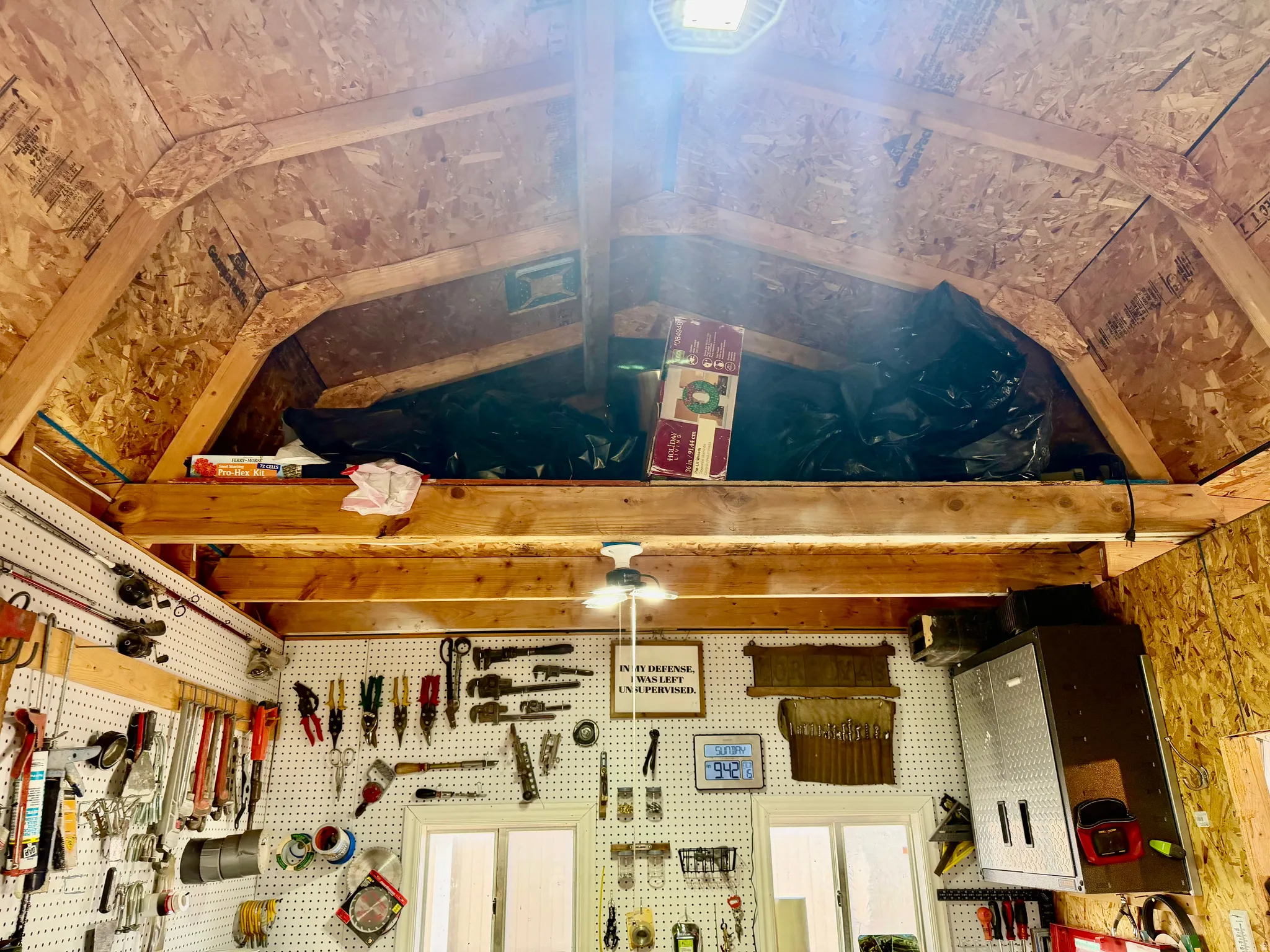Utility shed interior featuring exposed wood-finish framing, a loft storage area, and pegboard walls