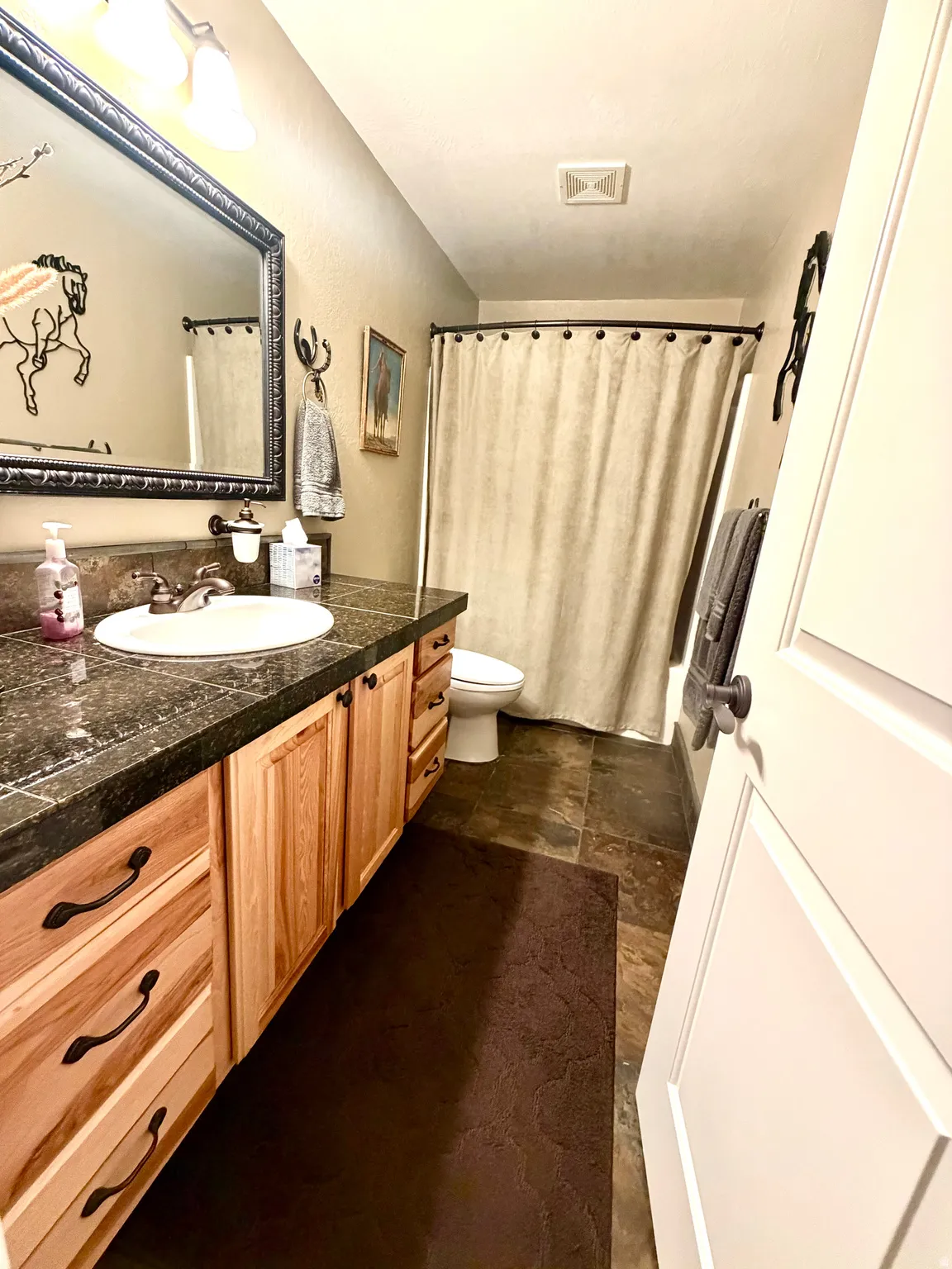 Bathroom featuring a natural wood vanity with dark hardware, a dark stone-finish countertop, and an undermount sink