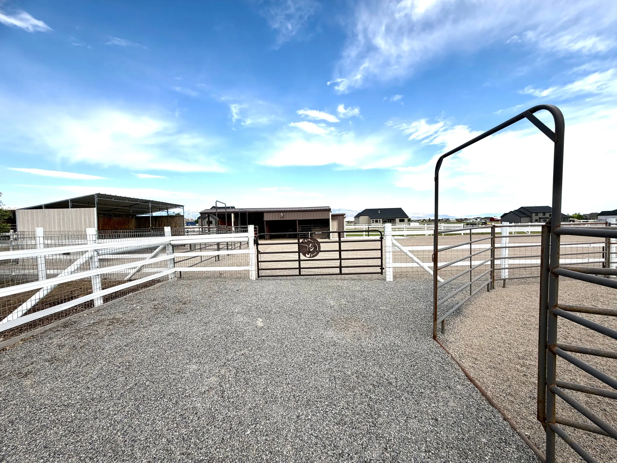 Gravel entrance area with a metal archway and white fencing, featuring a dark metal gate with decorative elements