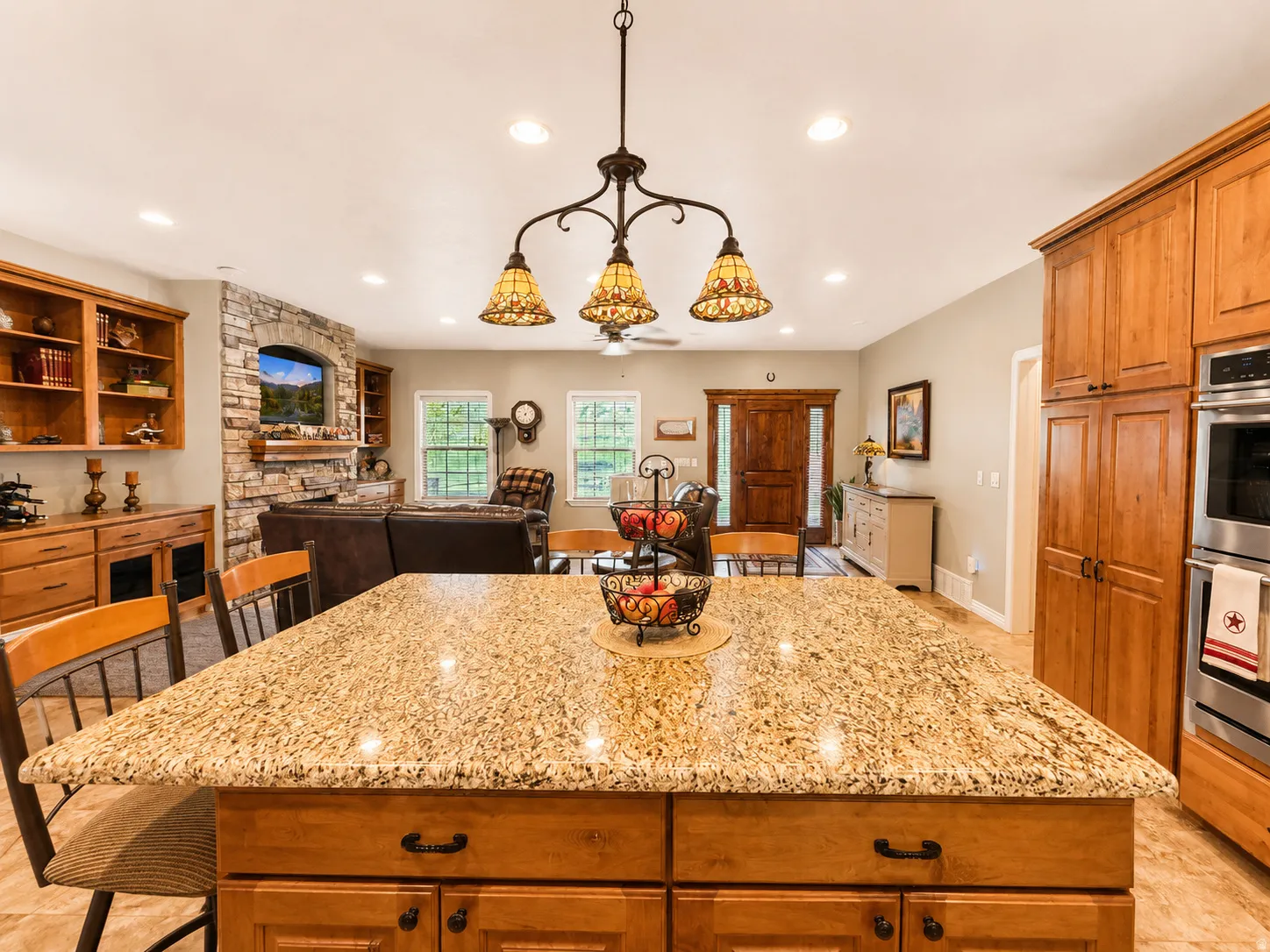 Spacious open-concept kitchen and living area featuring a large granite-topped island, light wood cabinetry, and stainless steel built-in appliances