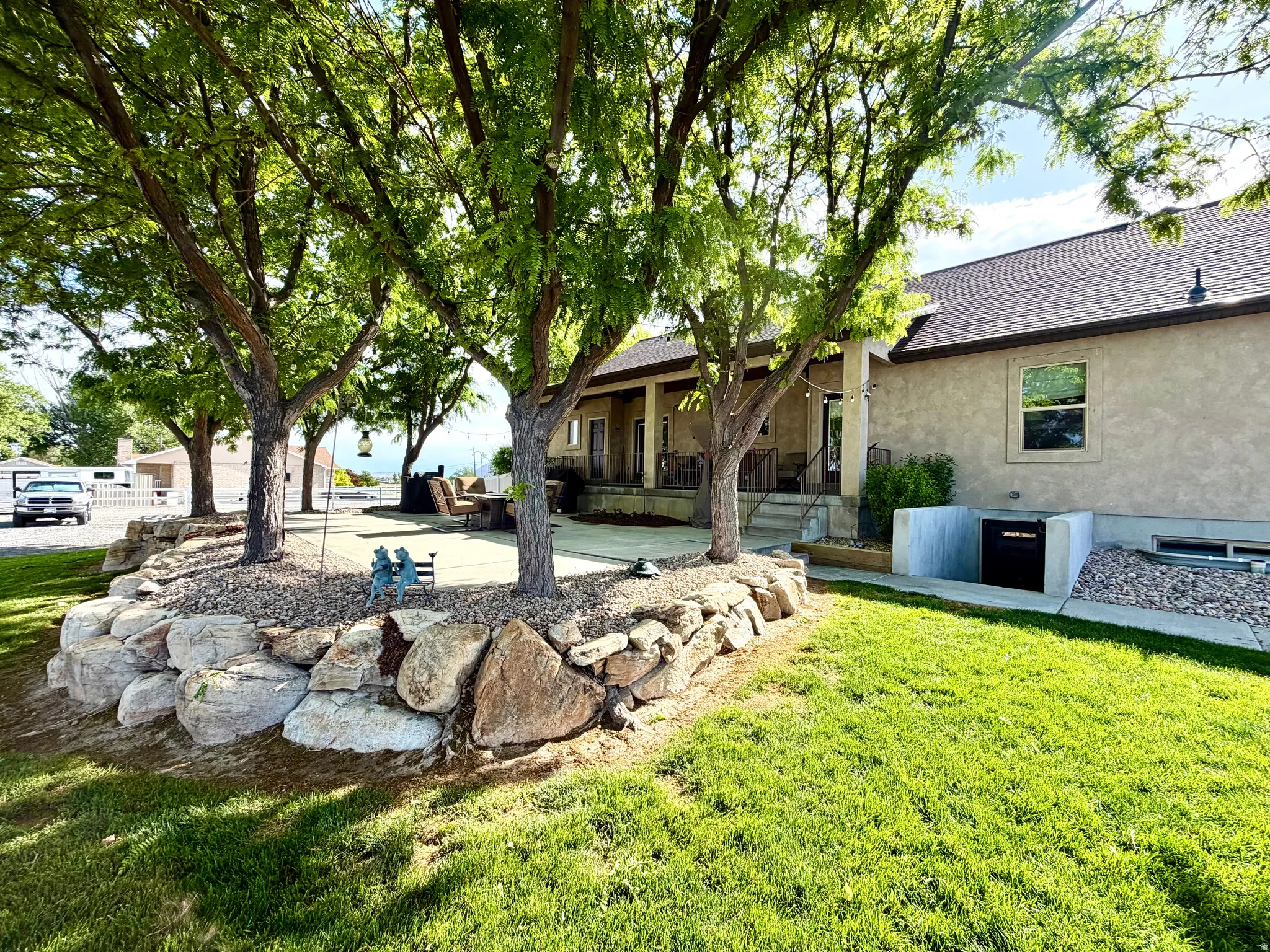 Expansive outdoor living area featuring a concrete patio, mature trees, and a rock retaining wall
