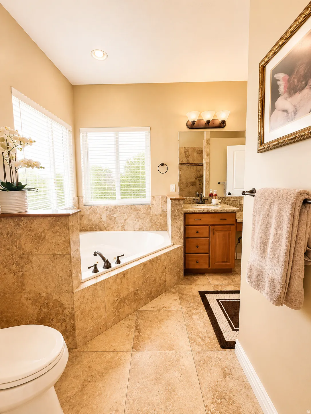 Bathroom featuring an integrated corner soaking tub with deck-mounted fixtures, a single vanity with wood cabinetry and a stone-look countertop, and large format tile flooring