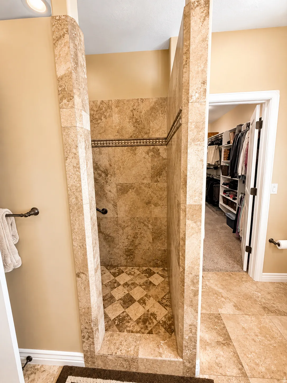 Walk-in shower featuring full-height natural stone tiling, a decorative border, and a contrasting checkered floor pattern