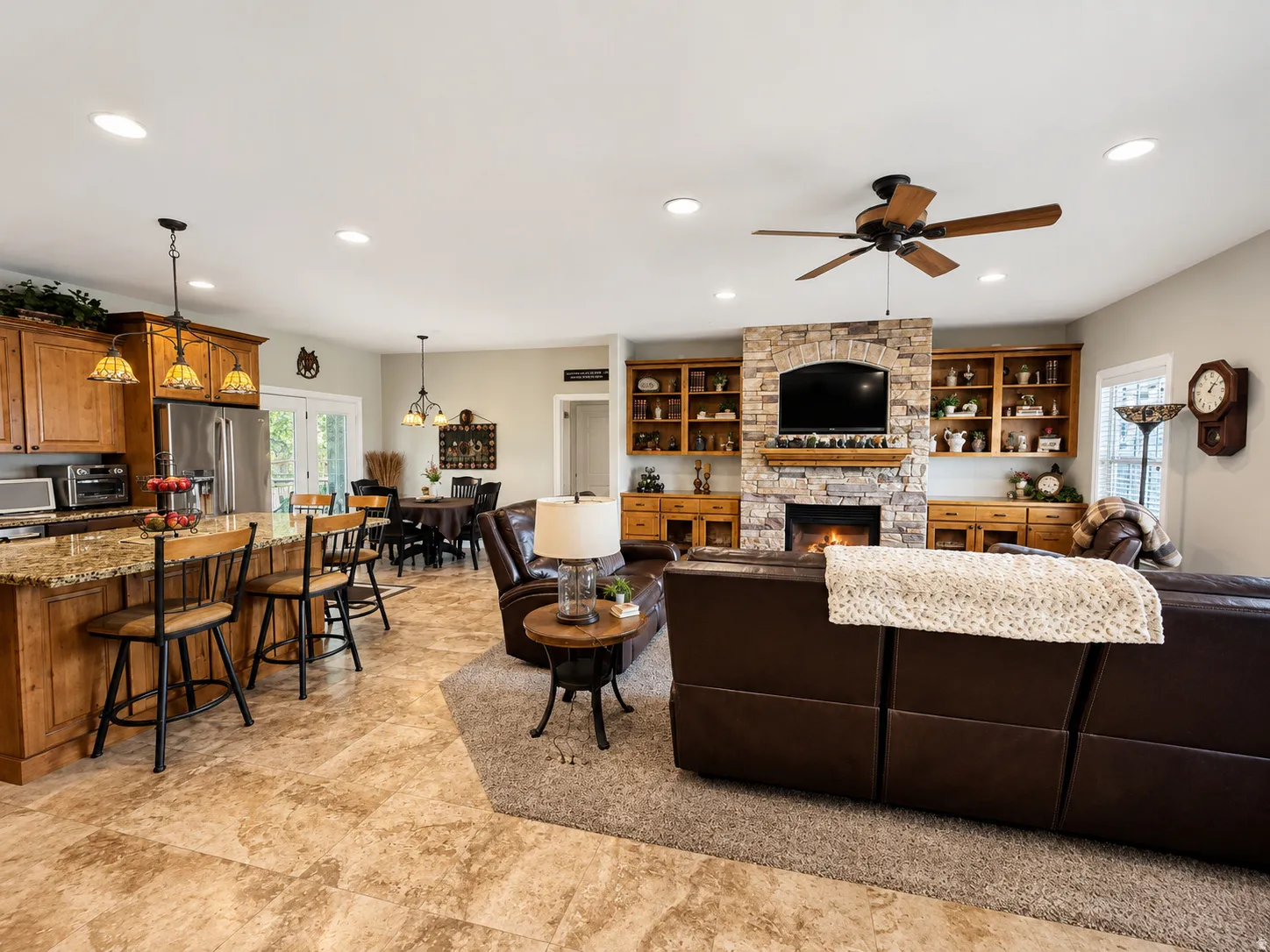 Expansive living area featuring a stone-clad fireplace, integrated shelving, wood-finish cabinetry, recessed lighting, and a ceiling fan