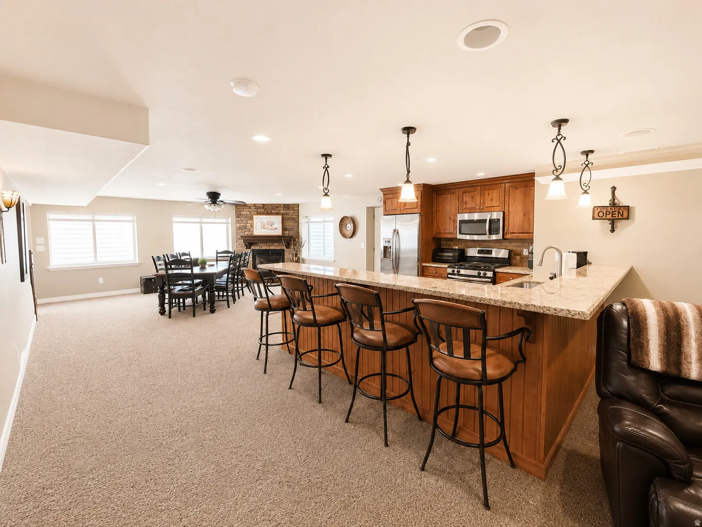 Lower-level entertainment space featuring a full kitchen with wood cabinetry, light-toned countertops, and stainless steel appliances