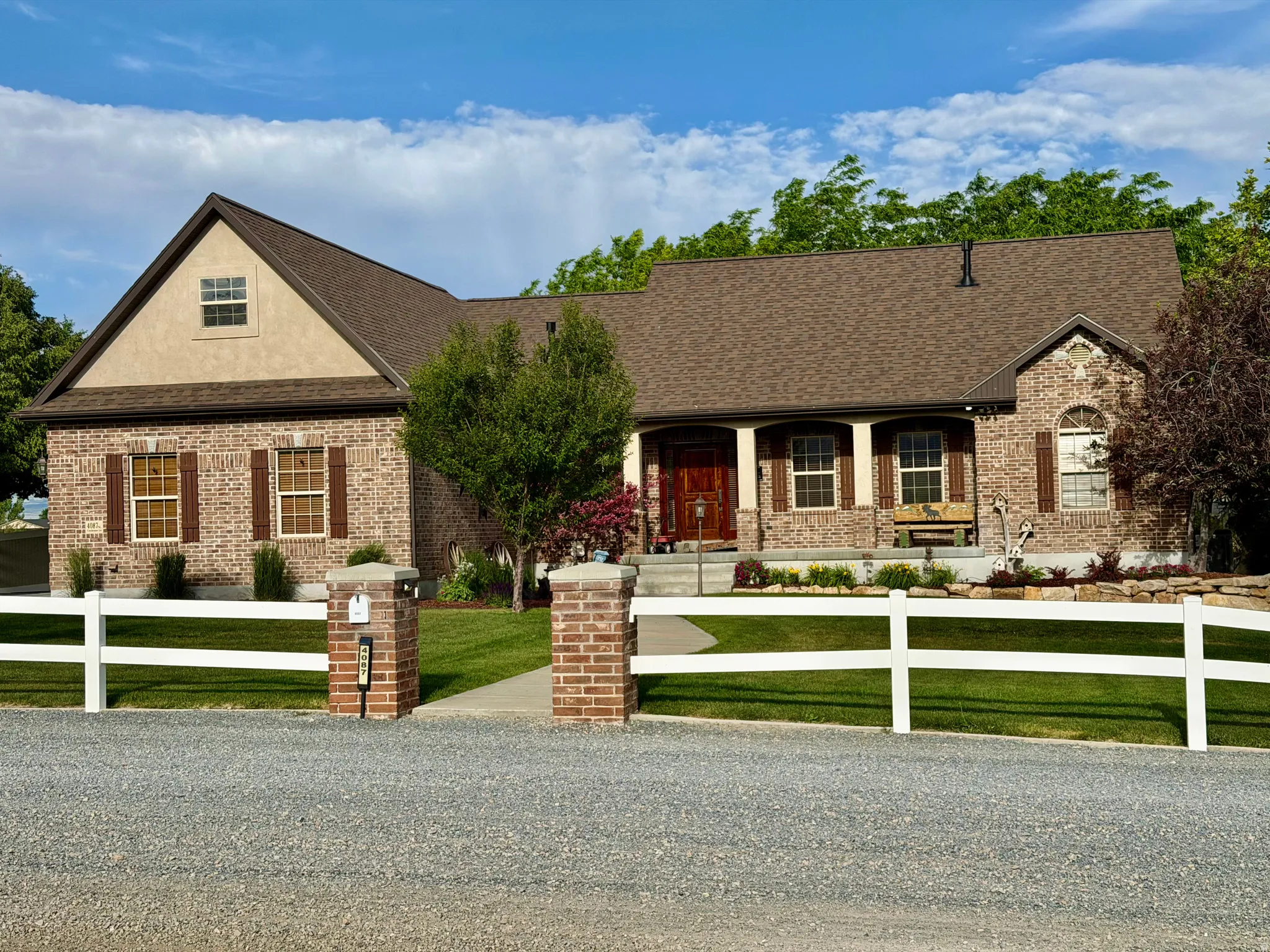 Brick and stucco exterior featuring a covered front porch with columns, a prominent front gable, and a driveway with a white fence