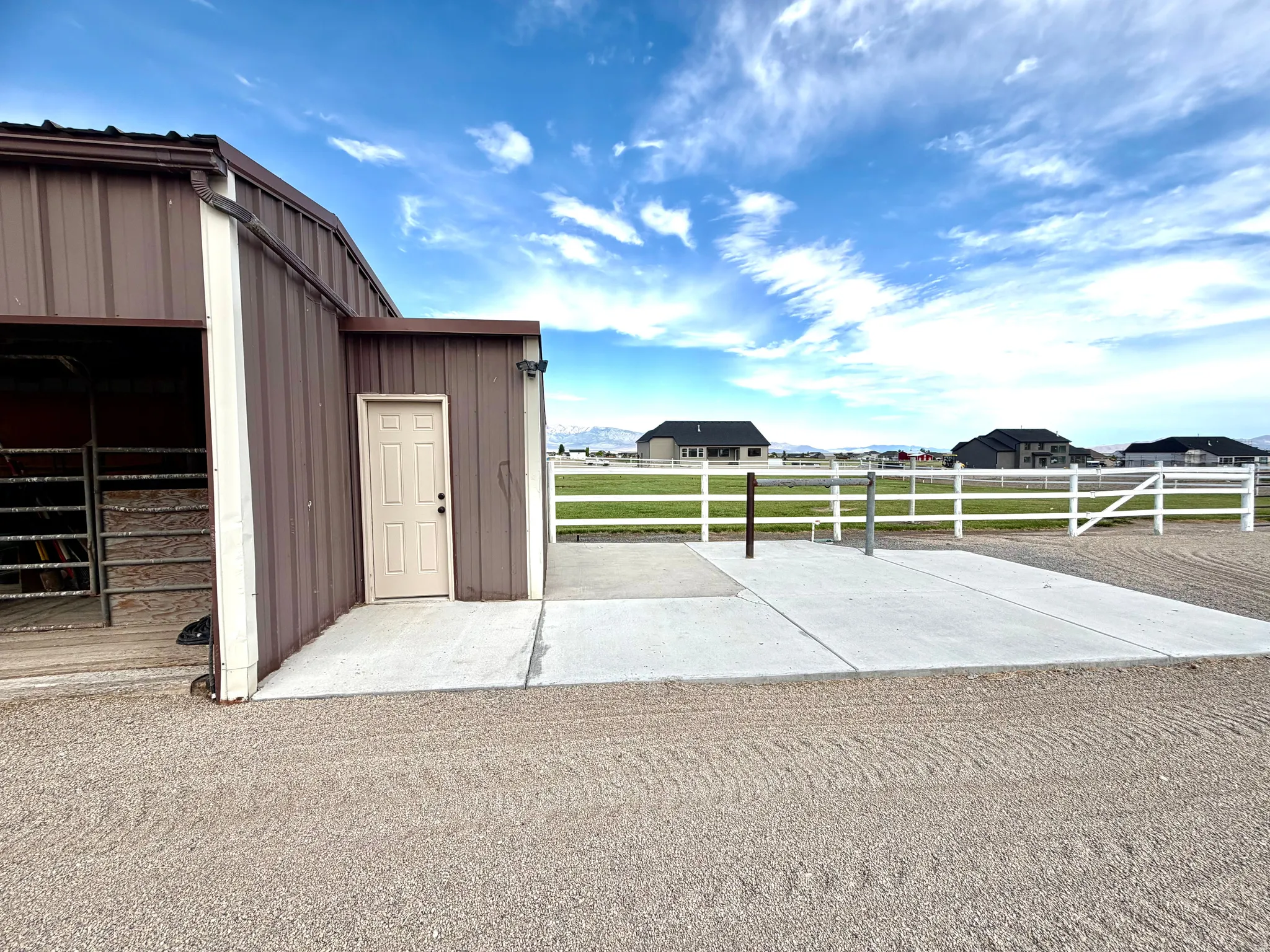 Metal-sided outbuilding with a tan access door, concrete pad, and adjoining gravel area