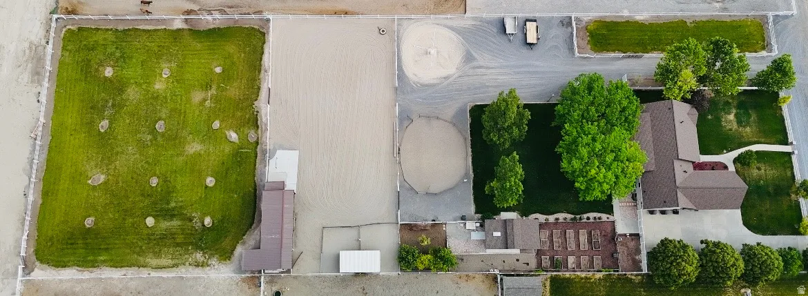 Expansive property featuring a main residence with brown roofing, multiple outbuildings, a large rectangular green space, and two circular sand areas