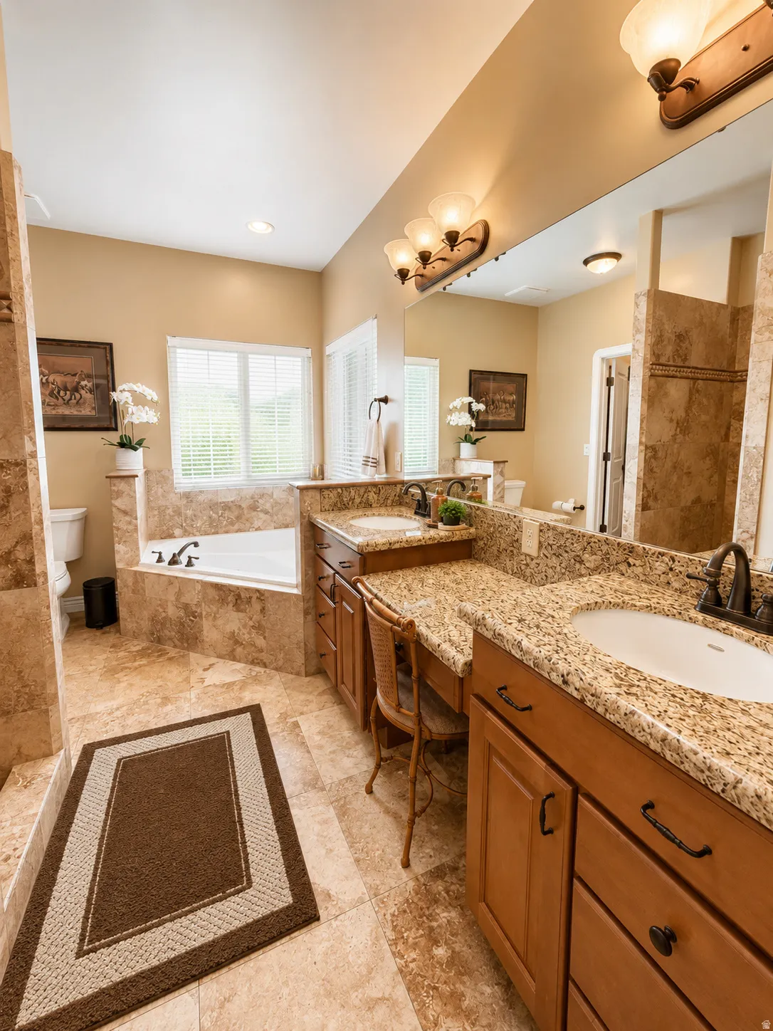 Bathroom featuring dual vanities with granite countertops, a built-in makeup area, a tiled walk-in shower, a built-in soaking tub, and natural light from a large window