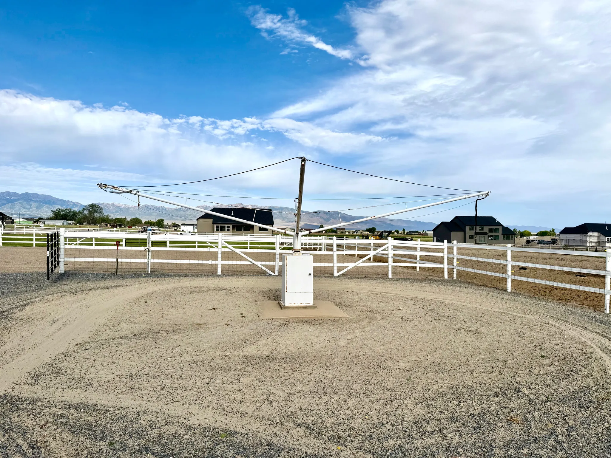 Enclosed equestrian arena featuring a white three-rail fence, a central training apparatus, and a gravel surface