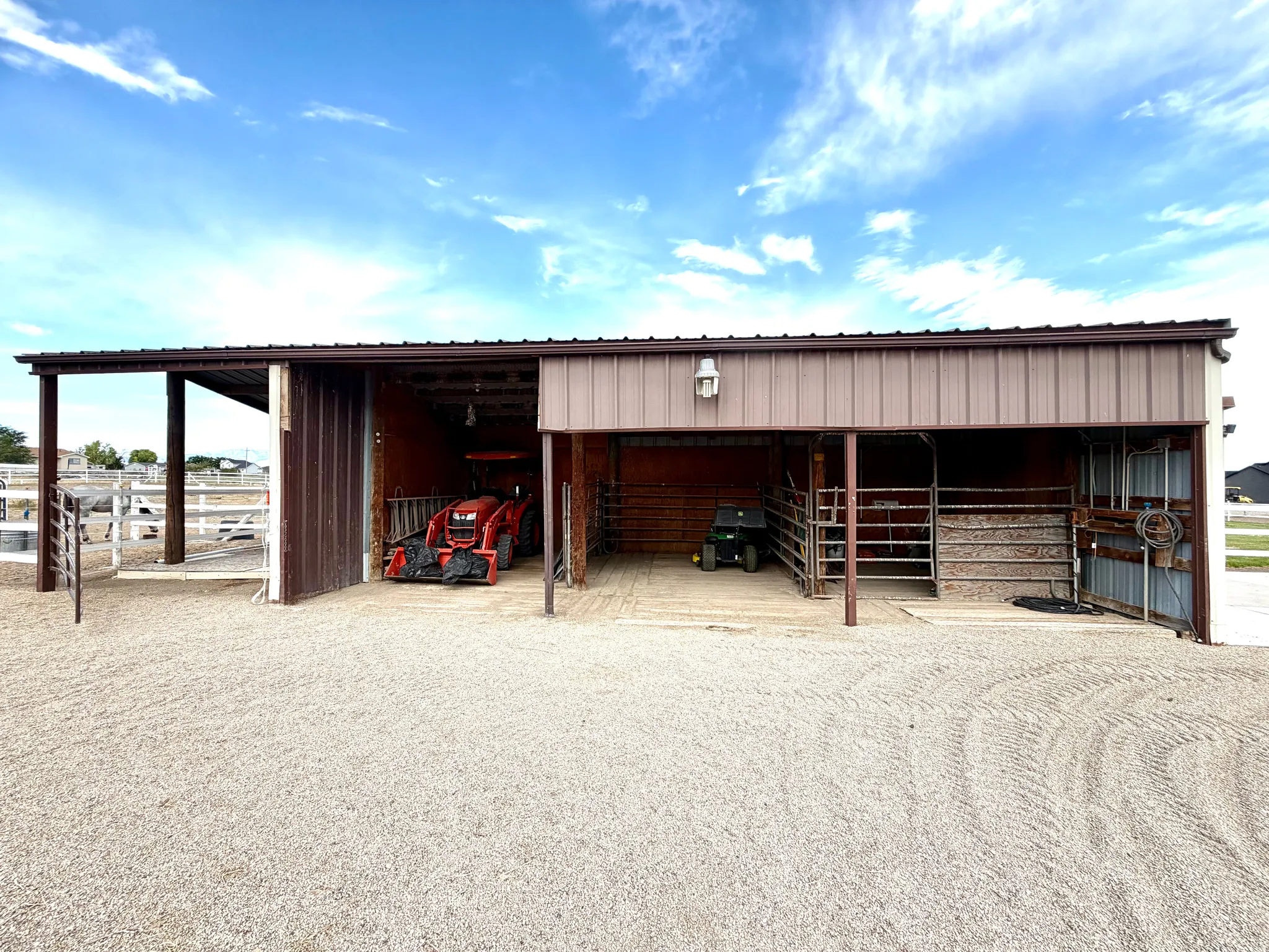 Metal-sided barn featuring a covered overhang, multiple bay openings, and interior lighting fixtures