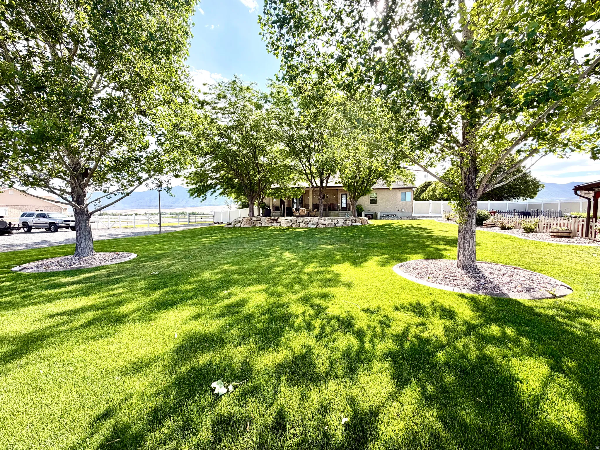 Spacious lawn featuring mature trees with rock and mulch beds, a fenced perimeter, and a covered back patio
