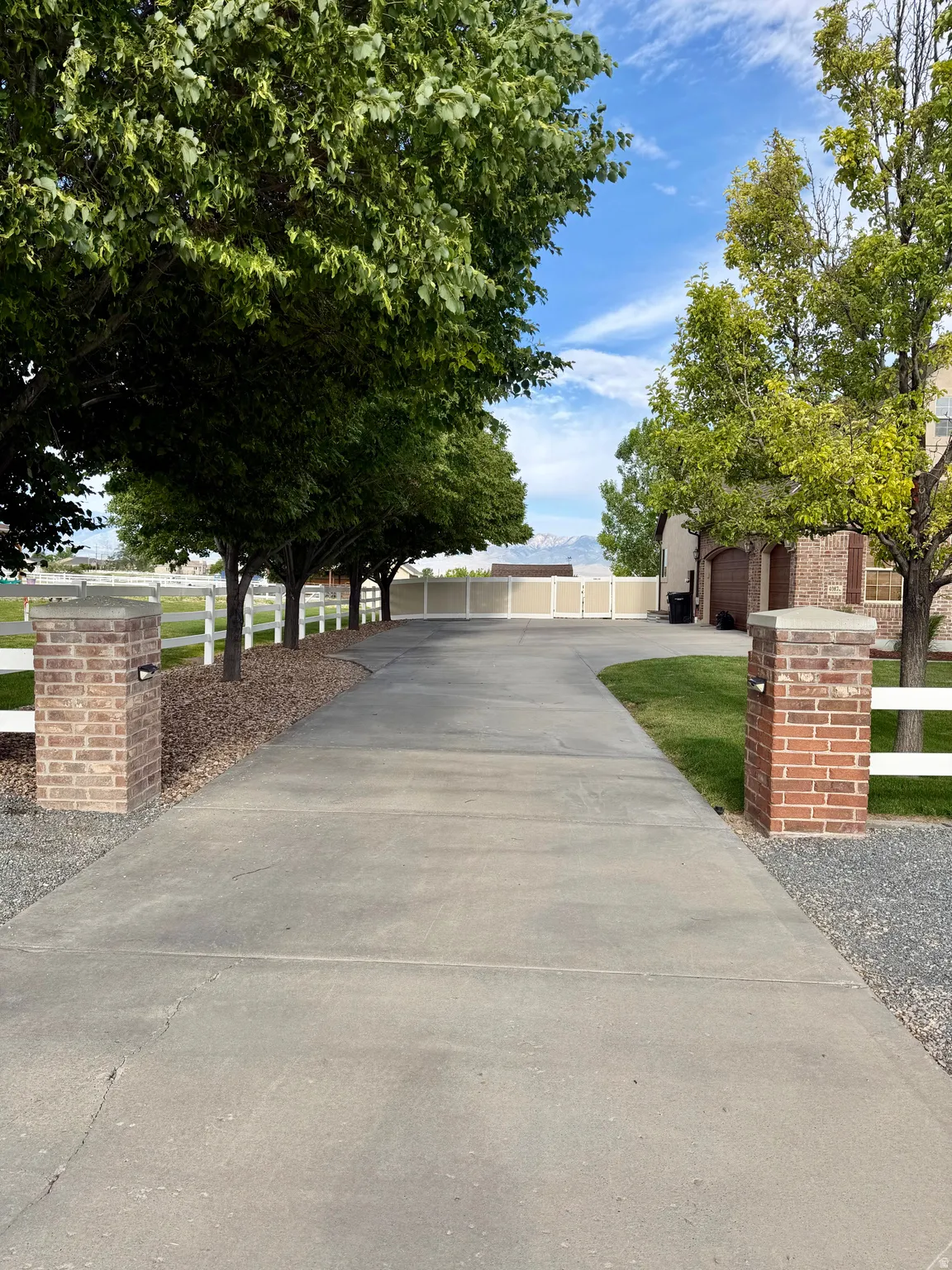 Expansive concrete driveway flanked by mature trees and a white picket fence