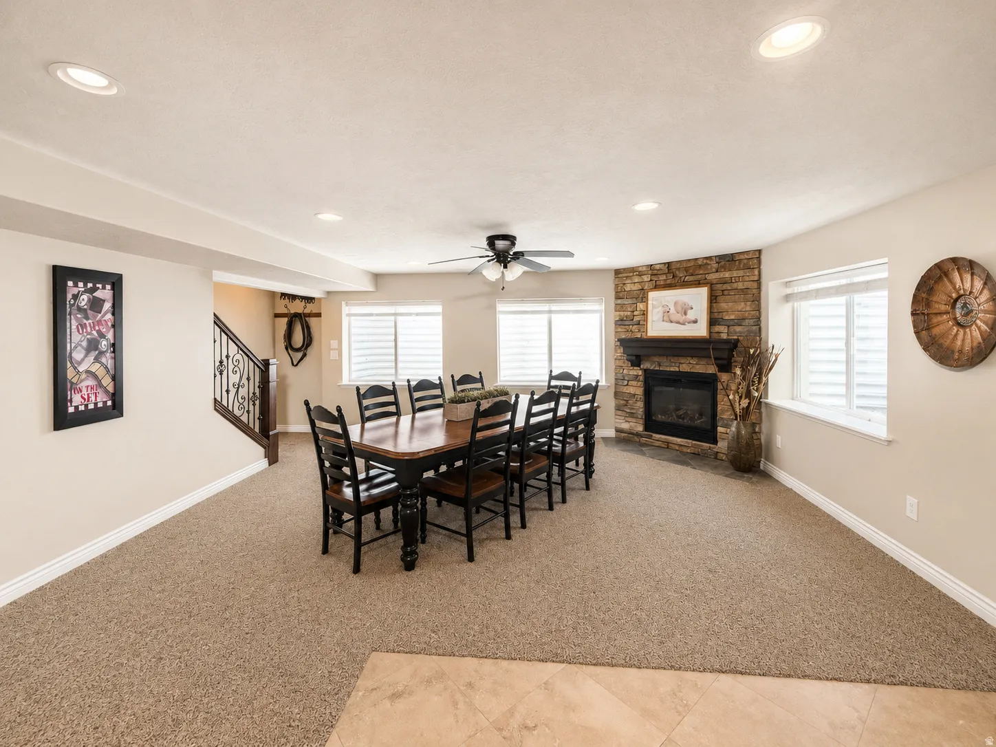 Carpeted living space featuring a stone-clad fireplace with a dark wood mantel, recessed lighting, and multiple windows with blinds