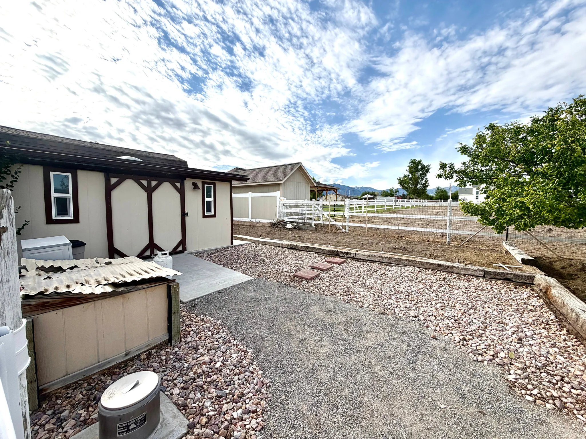 Accessory structure with dual-pane windows and a covered entry, concrete patio, gravel pathways, and white perimeter fencing