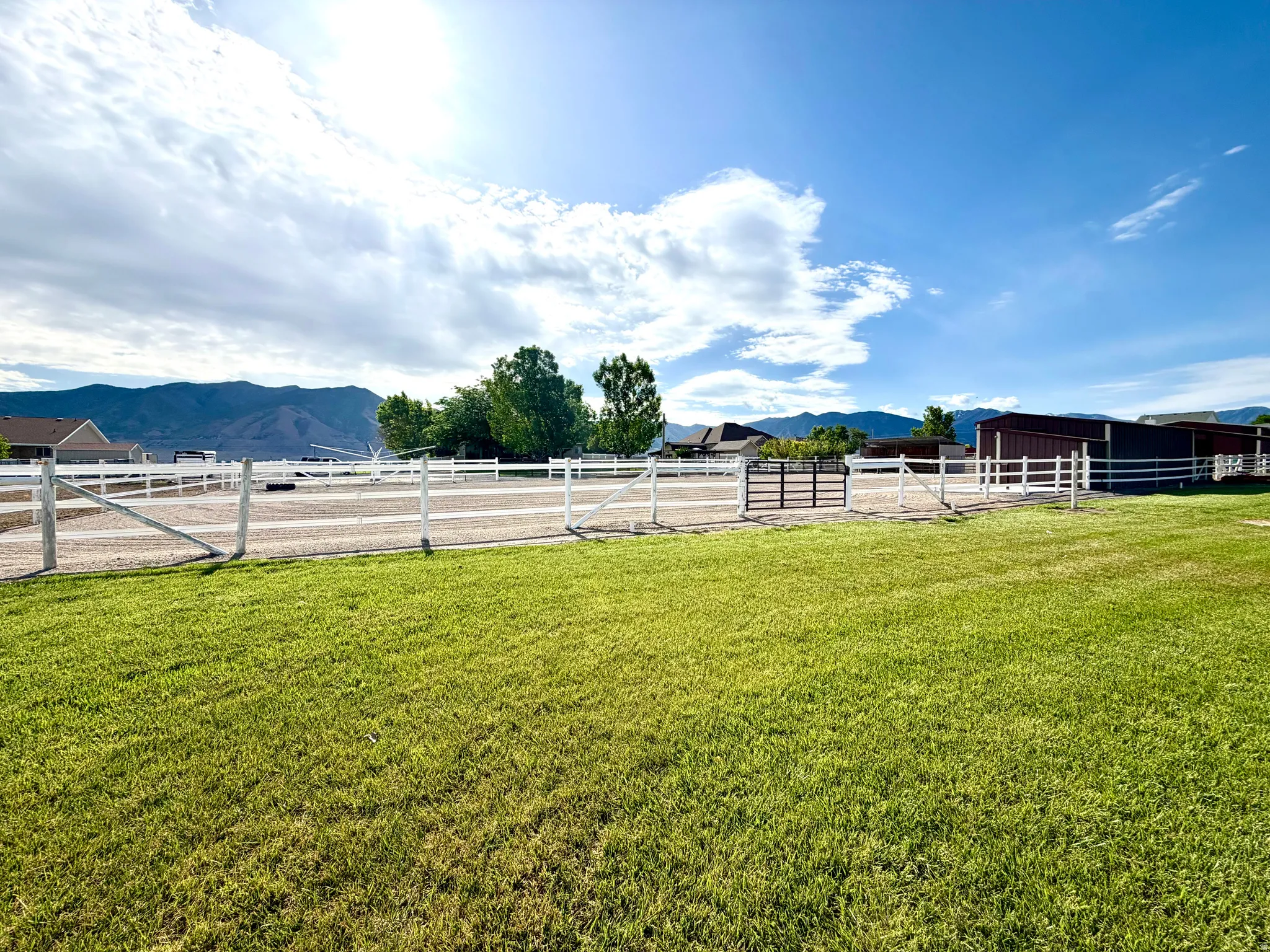 Expansive green lawn with a white fence enclosure surrounding a gravel arena