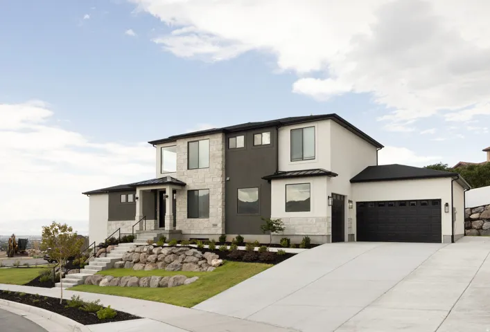 Modern stucco and stone facade featuring a prominent two-car garage, concrete driveway, and tiered landscaping