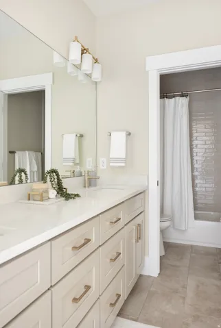 Double vanity featuring light-toned cabinetry with gold-toned hardware and white countertops