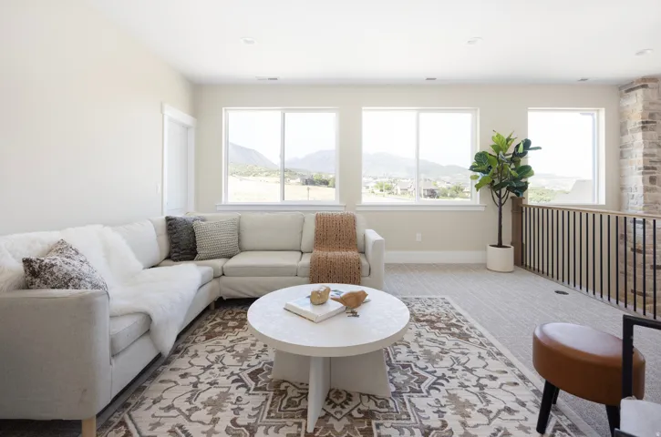 Upper-level bonus room featuring five large windows, light-colored carpeting, a stone-clad wall accent, and a black metal and wood railing