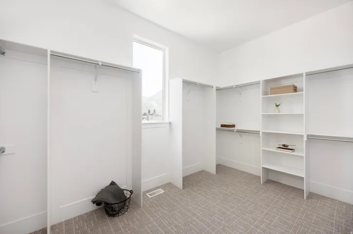 Spacious closet featuring built-in shelving, multiple hanging rods, and a large window