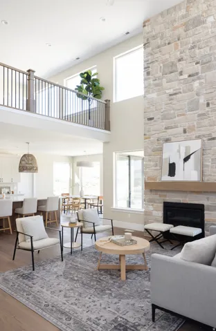 Two-story living area featuring a stone accent wall with an inset fireplace, a wood mantel, and large windows
