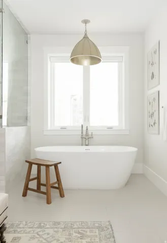 Freestanding soaking tub with brushed nickel floor-mounted faucet, set against a window with white trim
