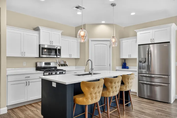 Gourmet kitchen featuring white shaker cabinetry, stainless steel appliances, a central island with a sink, pendant lighting, and wood-finish flooring