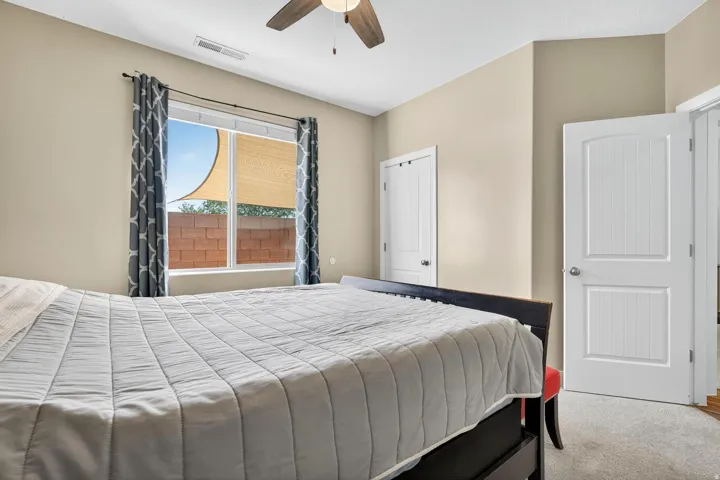 Bedroom featuring a large window with roller shades, neutral tone walls, and a ceiling fan with light fixture