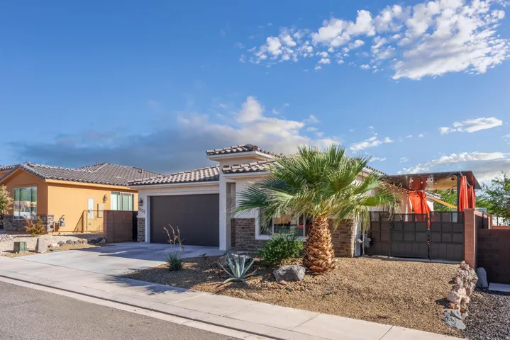 Contemporary stucco and stone exterior featuring an attached garage, tile roof, and desert-style landscaping