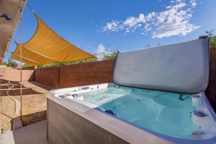 Outdoor spa with an open cover, surrounded by gravel landscaping, a block wall, and overhead shade sails