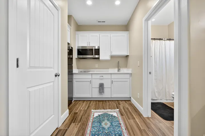 Compact kitchen area featuring wood-finish flooring, white cabinetry, integrated stainless steel microwave, and a single basin sink with a modern faucet