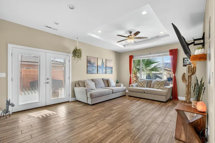 Spacious living area featuring wood-finish flooring, a tray ceiling with recessed lighting and a ceiling fan, and double patio doors