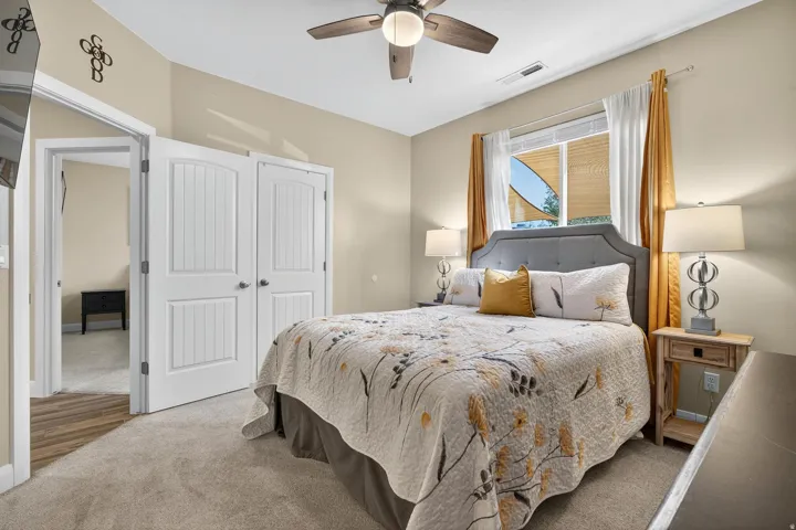 Carpeted room featuring a ceiling fan, window with blinds and drapes, and a doorway opening to wood-finish flooring