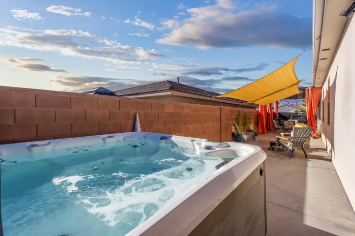 Outdoor spa with bubbling water, concrete patio, privacy wall, and a shade sail over an outdoor seating area