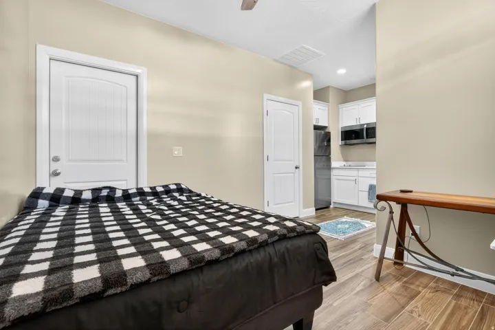 Compact living space featuring wood-finish flooring, light beige wall paint, a white paneled door, and a kitchen area with white cabinetry and stainless steel appliances