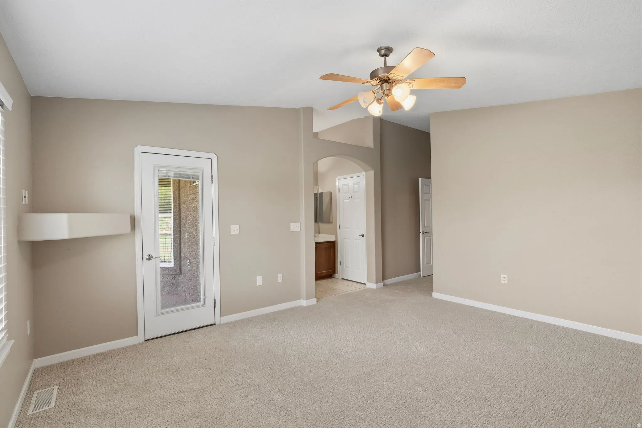 Spacious room with neutral carpeting and walls, featuring a glass-paneled door